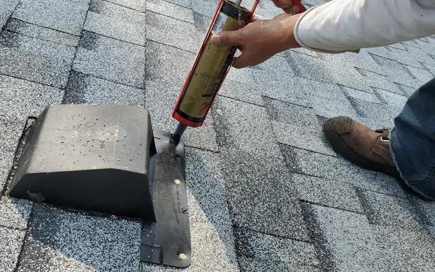Roofer applying caulking to seal exposed nails on vent